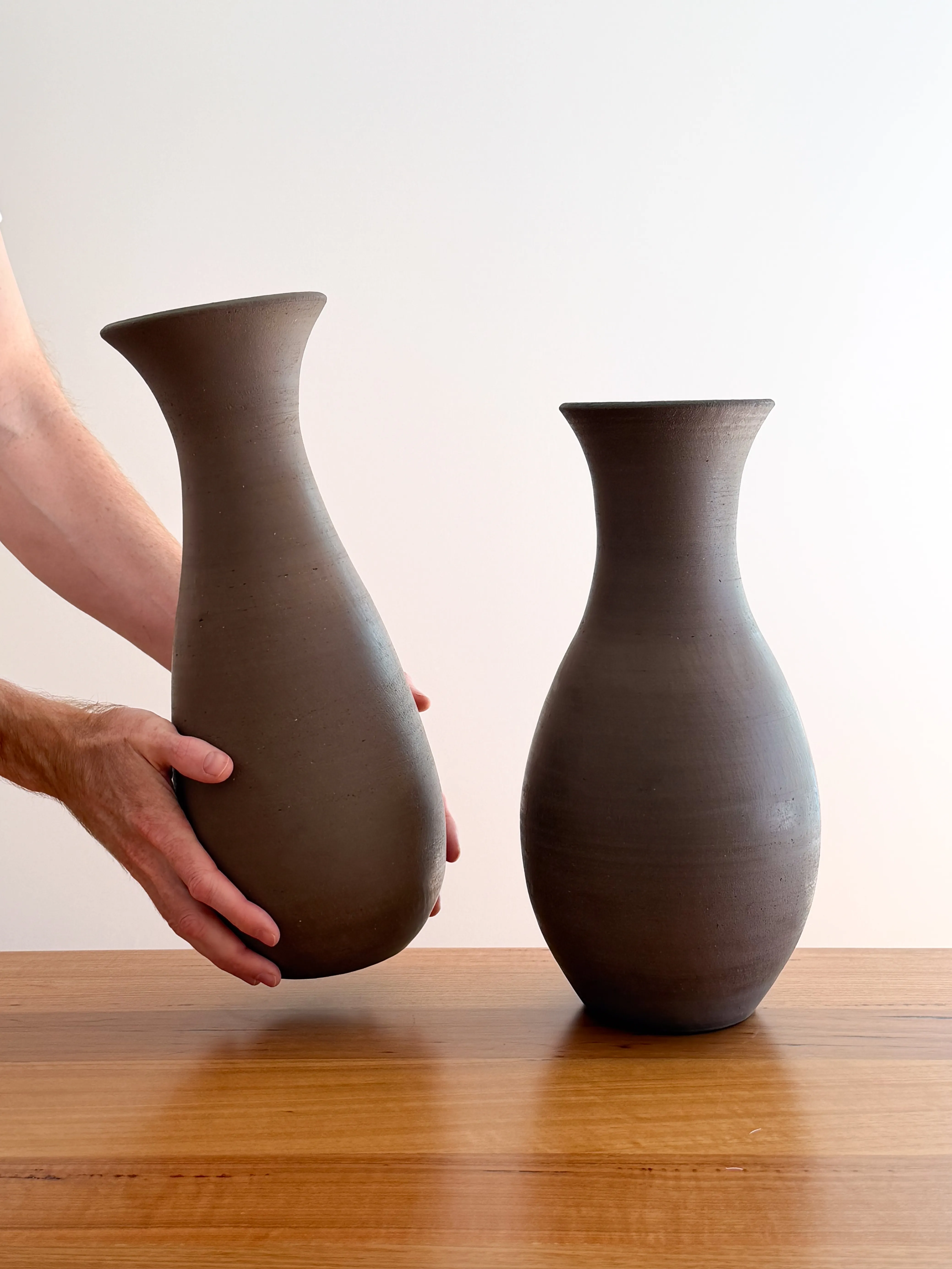Two tall dark stoneware bottle vases on a wooden bench