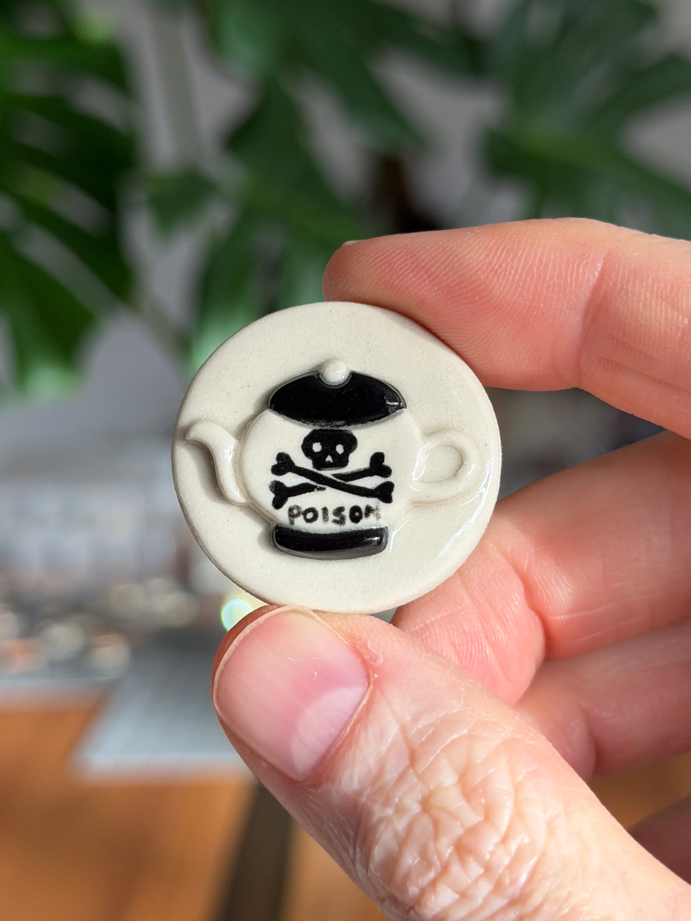Hand-sculpted ceramic brooch with a black skull-and-crossbones poison teapot design