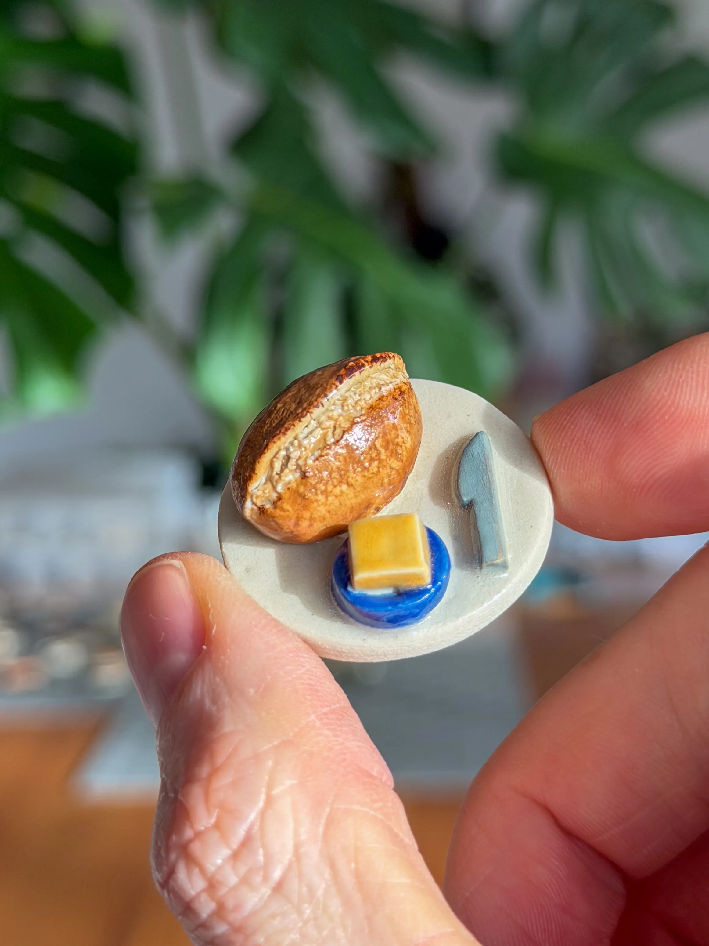 Hand-sculpted ceramic magnet of a bread loaf on a plate with butter and a knife