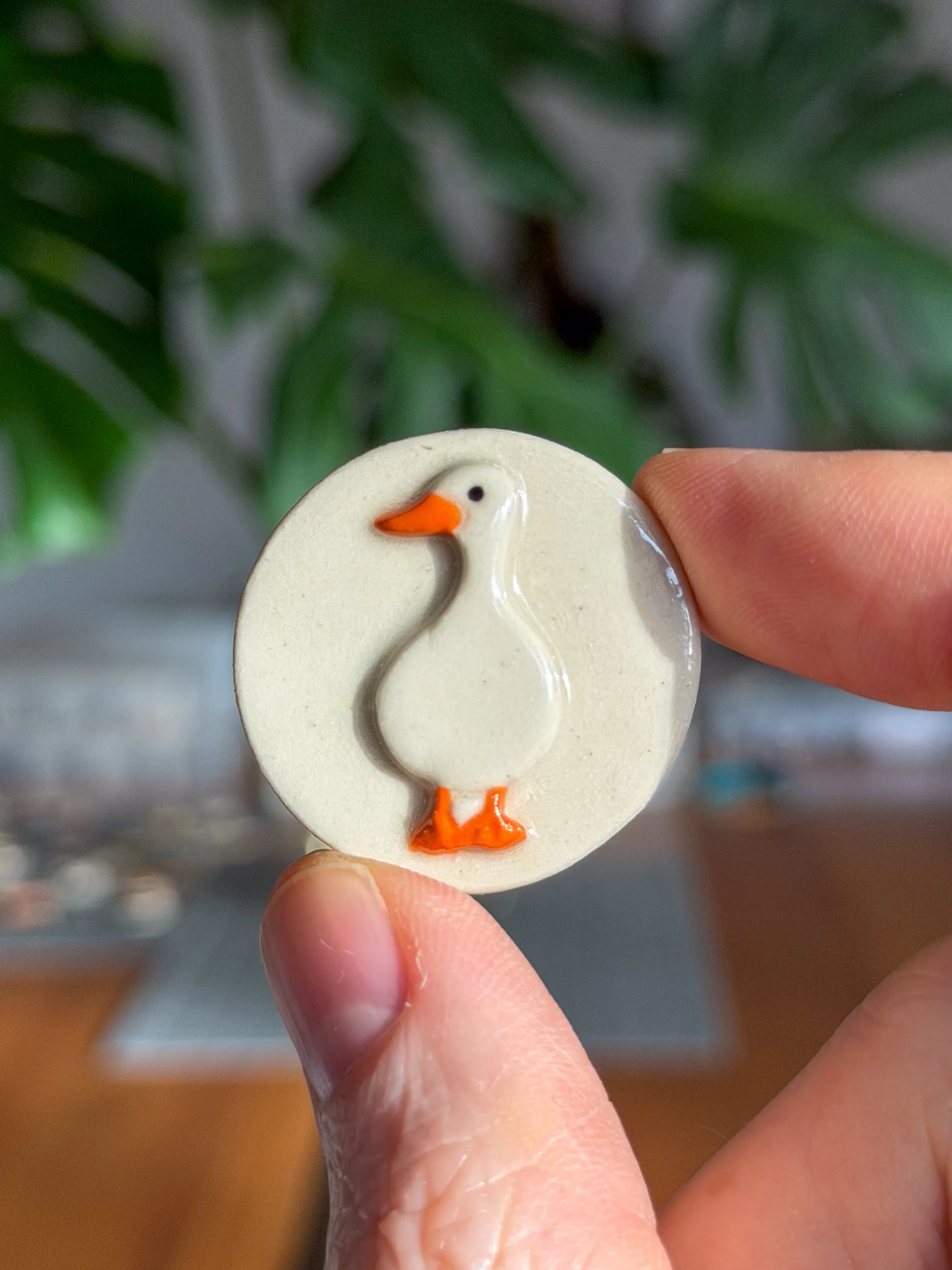 Hand-sculpted ceramic brooch of a white duck with an orange beak and feet