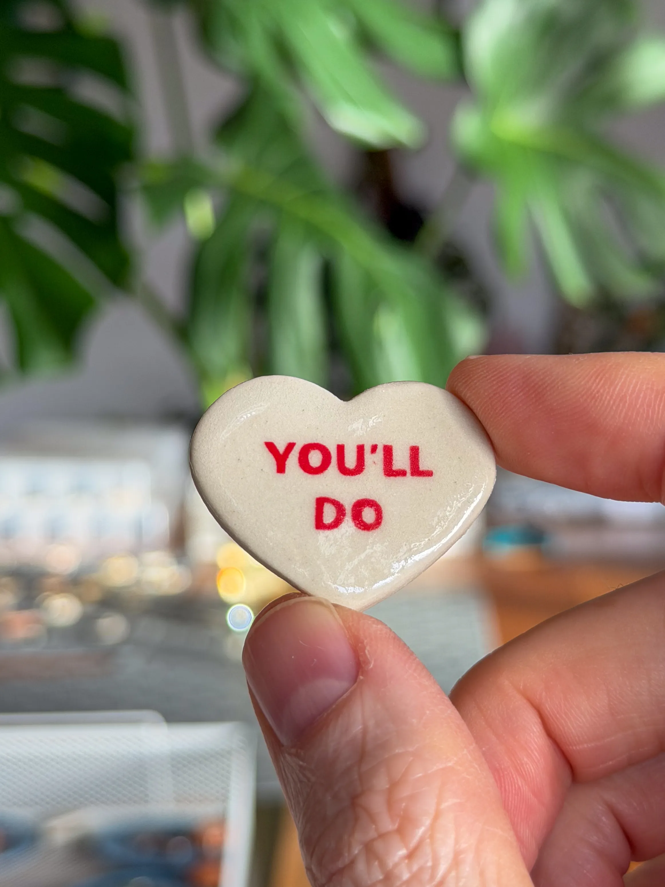 Heart-shaped ceramic candy-heart brooch reading You’ll Do in red