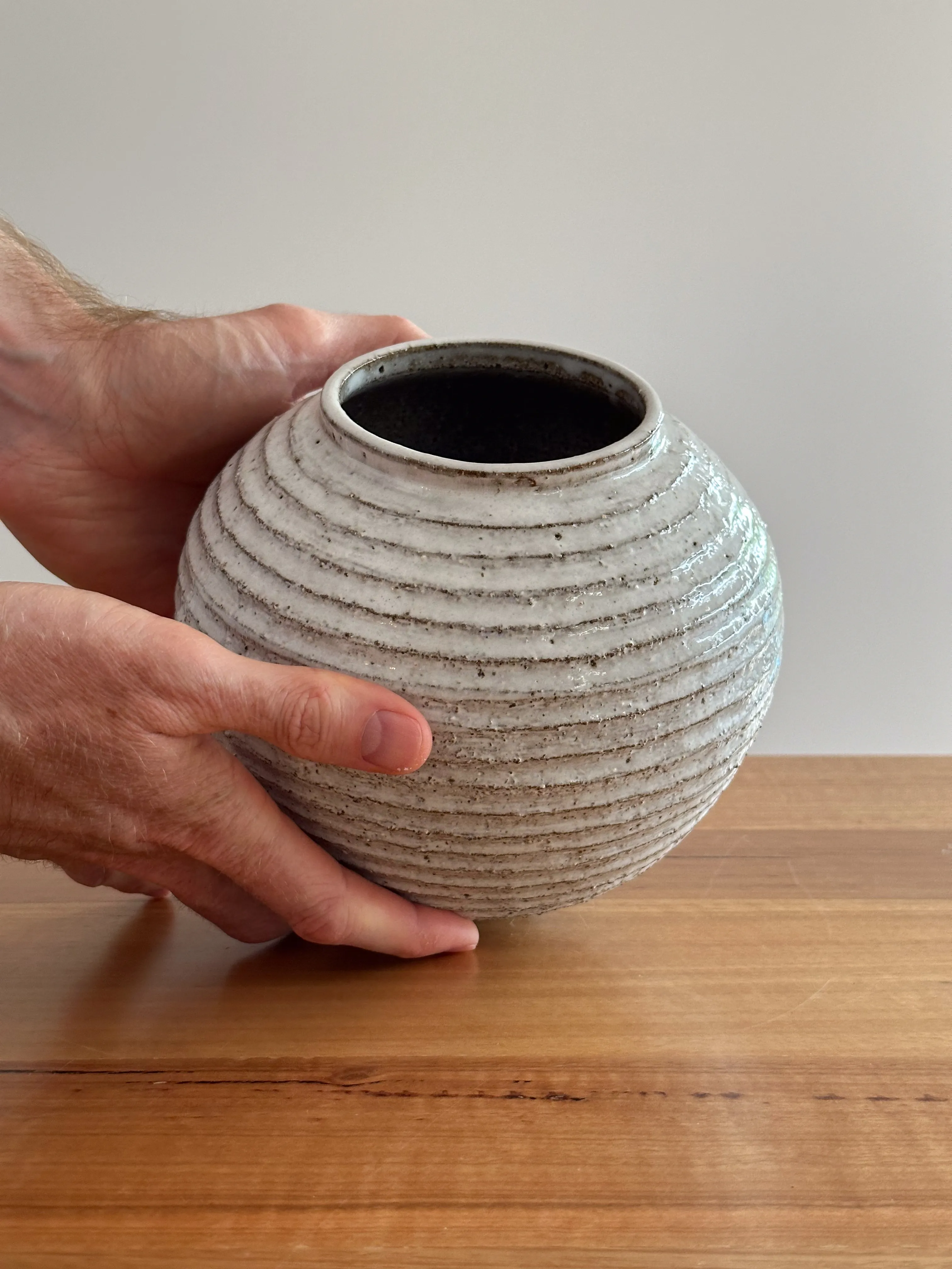 Spherical wheel-thrown stoneware vase with horizontal rib texture, held in a hand