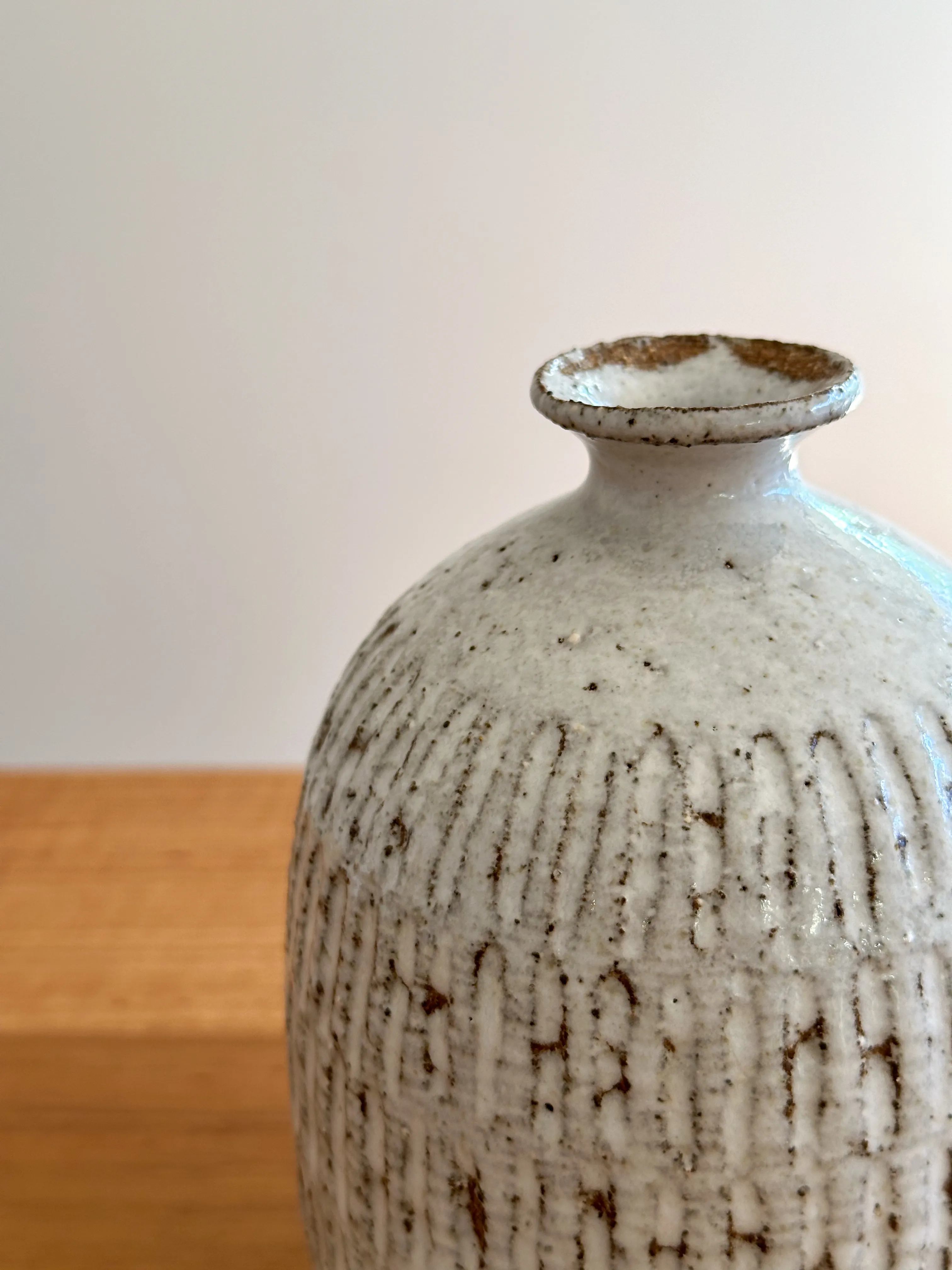 Close-up of a stoneware bud vase with fork-cut vertical texture and white glaze