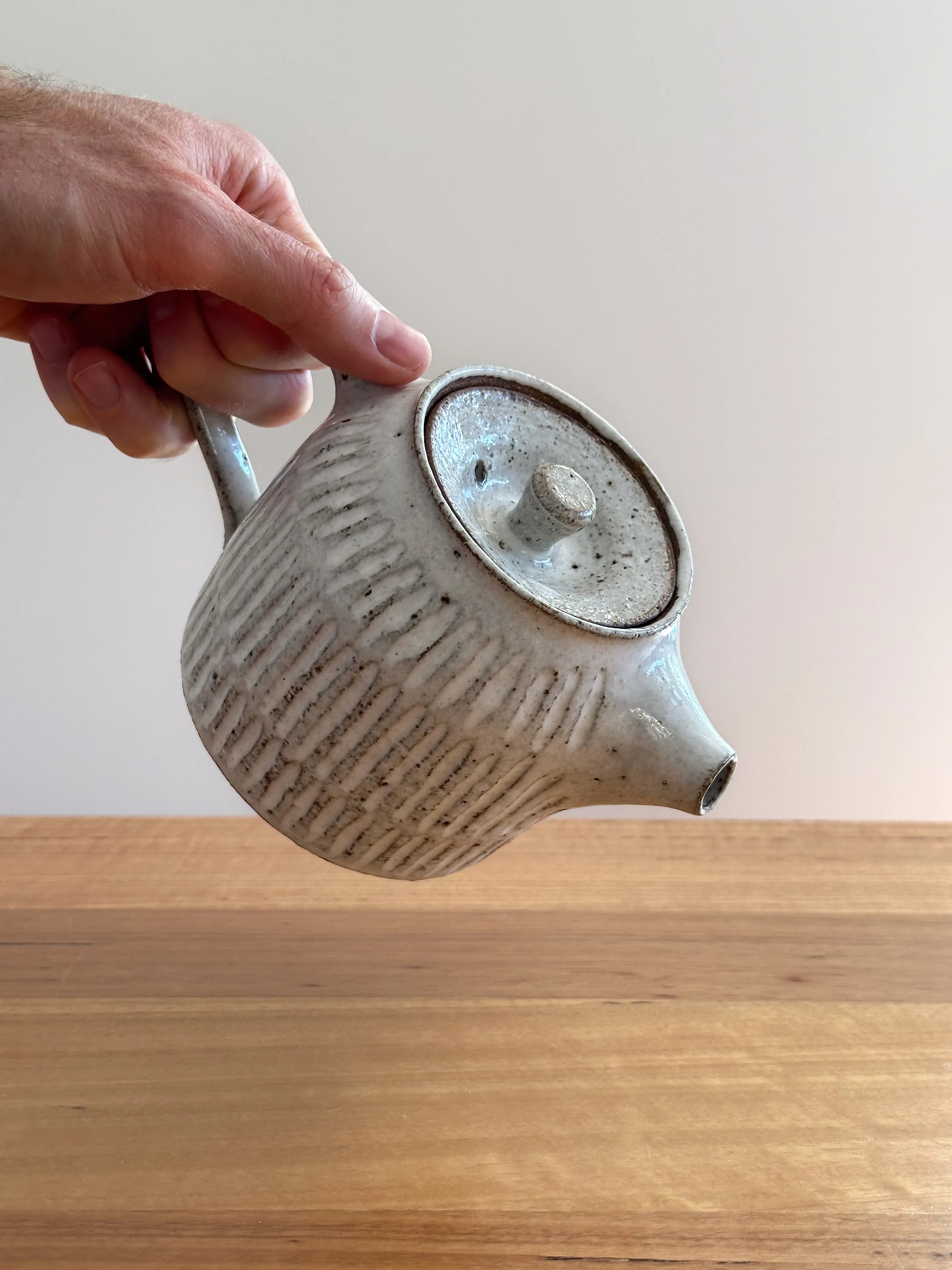 Wheel-thrown stoneware teapot held in a hand, fork-cut vertical texture and white glaze