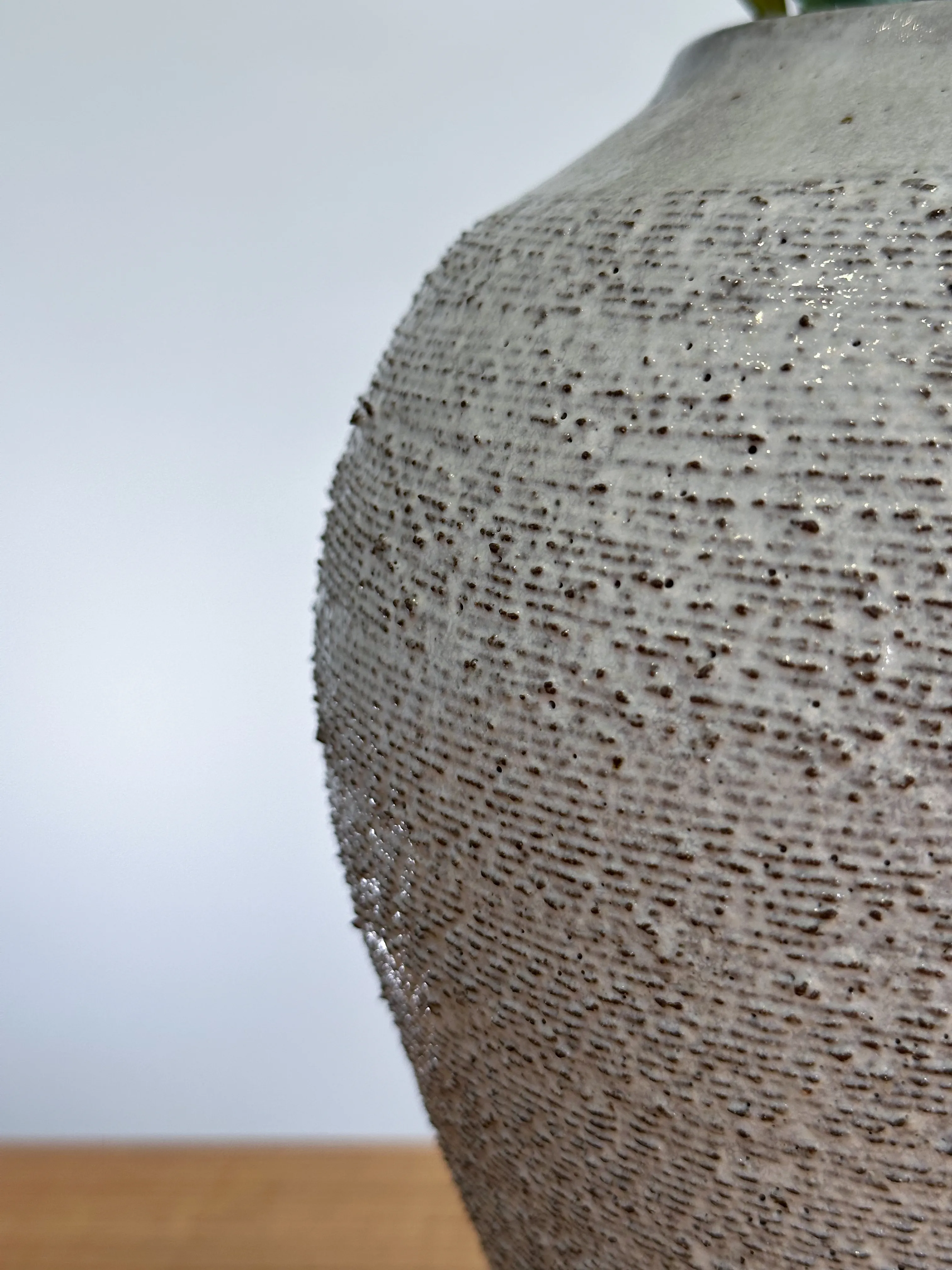 Close-up of speckled white glaze pooling over dark stoneware texture