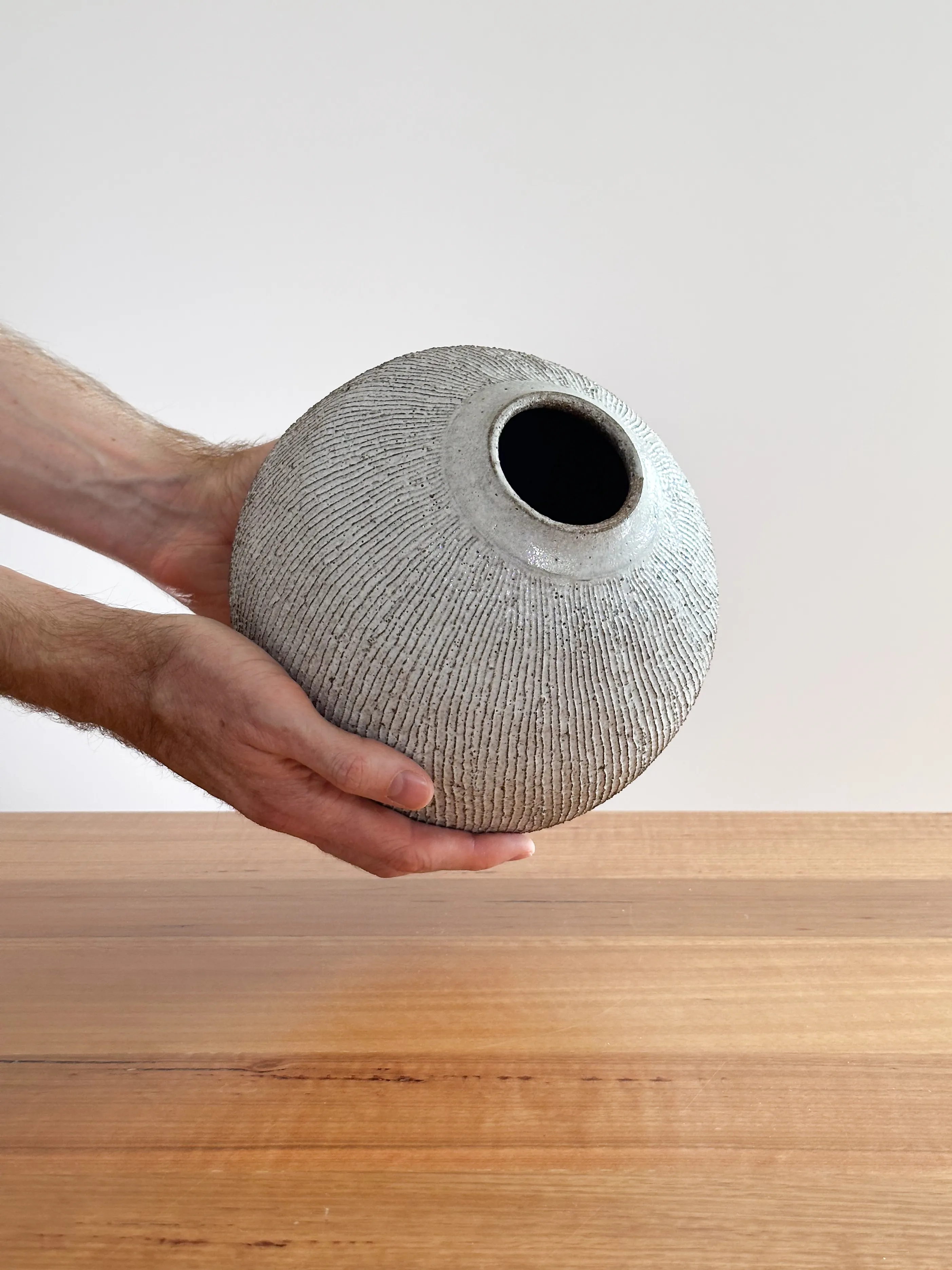 Round stoneware vase with vertical fork-cut texture and white speckled glaze, held in a hand