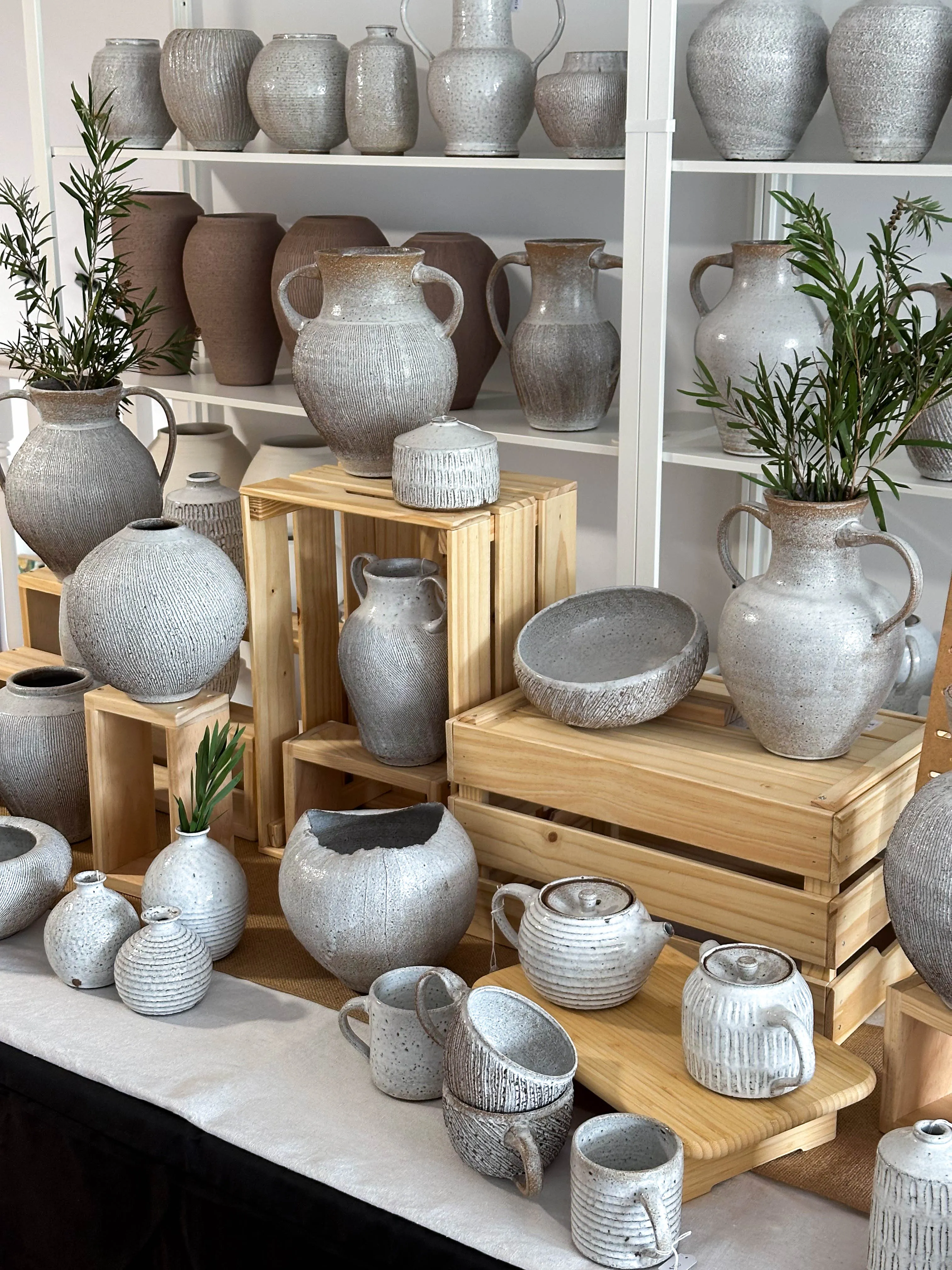 Stoneware pottery market display: vases, jugs, mugs and teapots on wooden shelves
